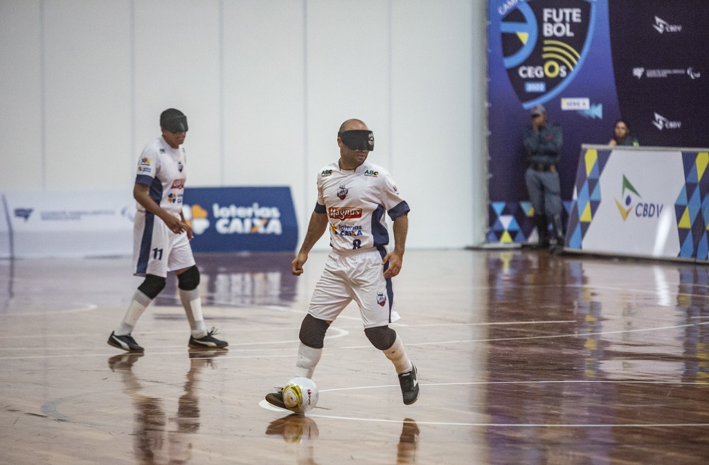 Daniel Iturra Adef Campeonato Brasileiro de futebol de cegos Daniel Iturra com a posse de bola em jogo do Adef-DF. Ele usa uniforme inteiramente branco. Ao fundo, há um jogador de sua equipe.