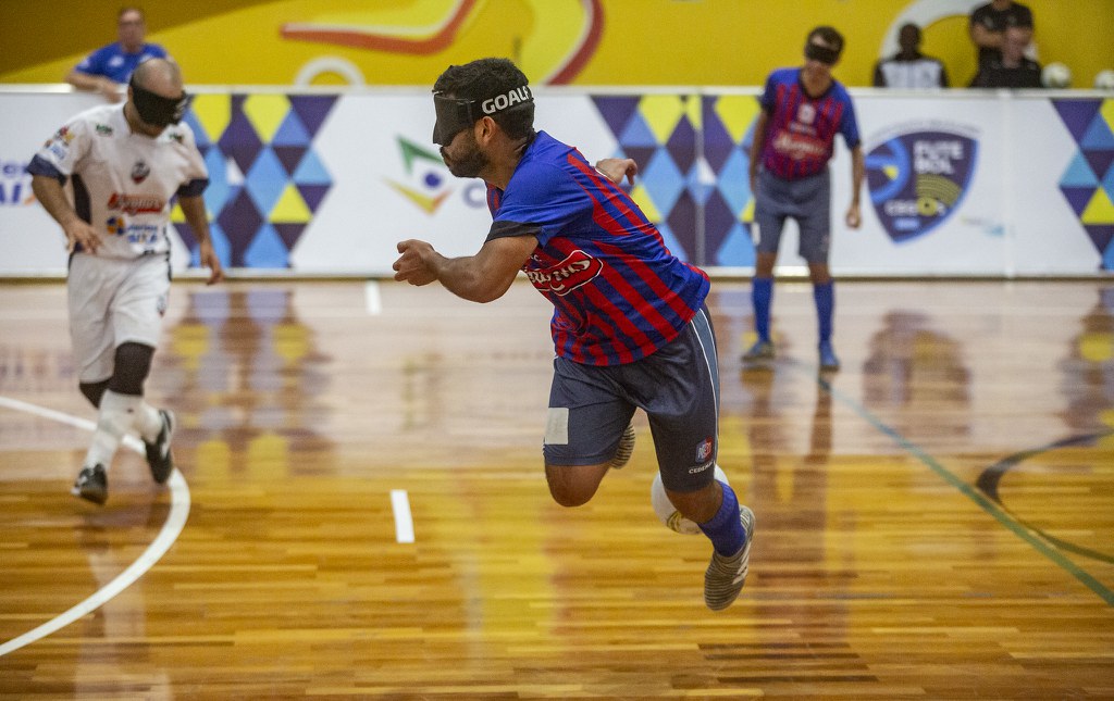 Victor Silva, da Cedamac, aplica carretilha em adversário Victor Silva, atleta da Cedamac, aplica carretilha em adversário da Adef. Ele usa camiseta vermelha com azul e está com a bola no ar.