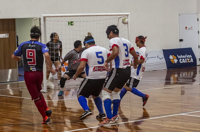 Jhon Gonzalez Apadevi Cedemac Brasileiro de futebol de cegos Jhon Gonzalez acerta chuta no ângulo, mesmo marcado por três defensores. O goleiro olha a bola.