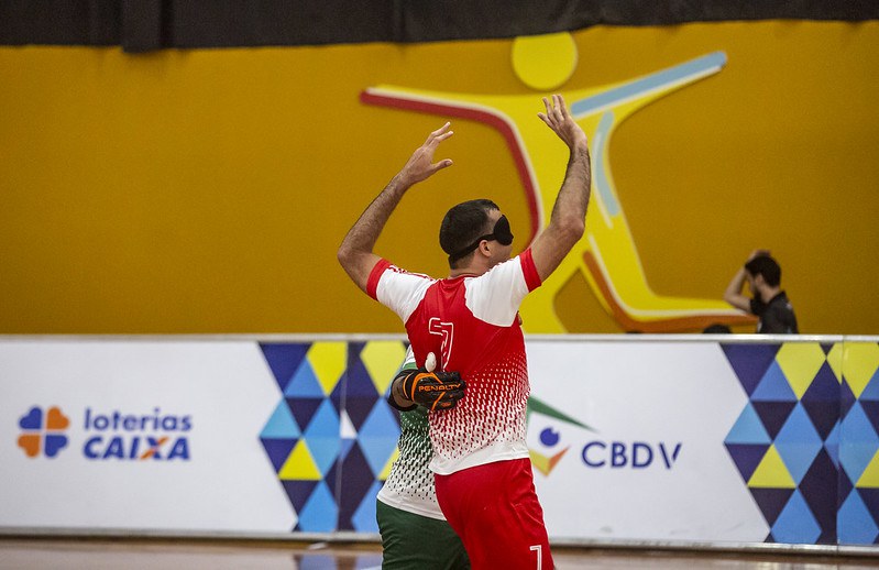 Derocy Escema x Adesul Campeonato Brasileiro de futcegos Derocy, de uniforme vermelho, comemora gol abraçado ao goleiro do Escema. Ele ergue os braços e vibra.