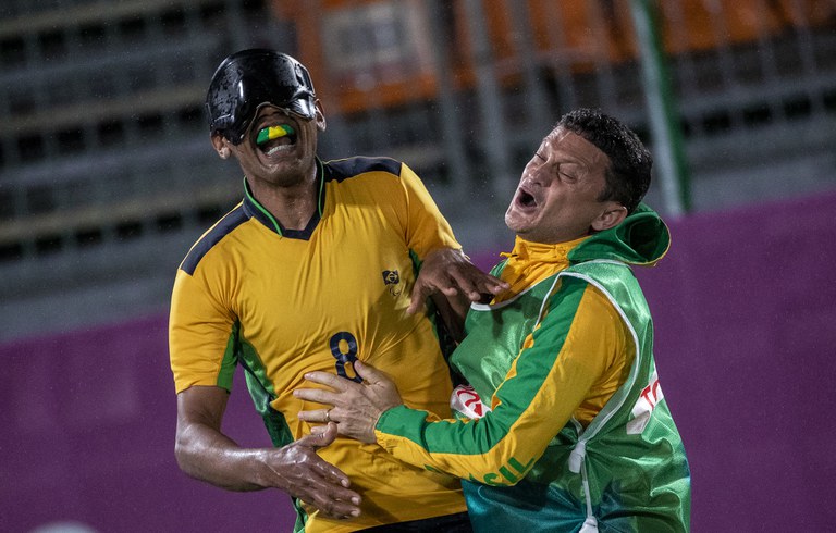 #Acessibilidade: Nonato comemora o gol na final abraçado ao chamador Edson Jr. Jogador veste camisa amarela com o número 8 escrito em verde.